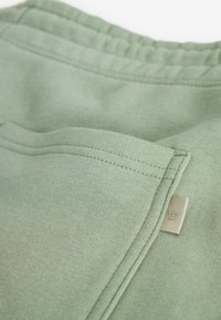Pantalons de sport en coton vert clair avec une surface texturée, une taille élastique et une petite étiquette de marque sur le côté.