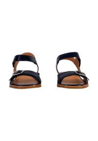 Sandali neri in pelle con due cinturini paralleli e un accento circolare in argento. Suola piatta con interno marrone e design aperto per la traspirabilità.