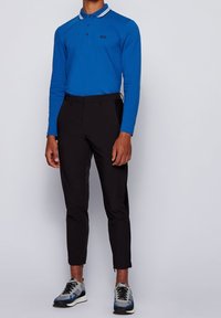 Blå långärmad polo med vita krageaccentuerade detaljer, kombinerad med svarta slim-fit byxor och grå, blå och svarta sneakers med snörning.