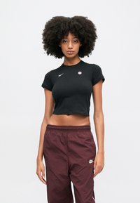 Crna skraćena majica od pamuka, s kratkim rukavima i bijelim Nike logotipom. Uparena s maroon Nike trenirkama.