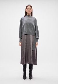 Γκρι μαλλινό πουλό�βερ με ψηλό λαιμό και χαμηλούς ώμους, φορεμένο πάνω από μια σατέν φούστα μέχρι το γόνατο σε ήπιους τόνους μωβ. Μαύρες μπότες μέχρι το γόνατο.