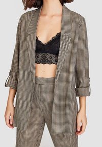 Blazer à carreaux marron et noir, à la coupe décontractée, avec des revers crantés et des manches retroussées, associé à un bralette en dentelle noire.