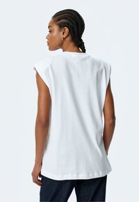 Hvid ærmeløs t-shirt med en let løs pasform, rund udskæring og blød bomulds tekstur, med afslappede skuldersømme.