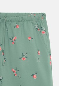 Grønt stoff med elastisk midjebånd som har et blomstermønster av røde ferskener og blader som er spredt rundt. Glatt tekstur.