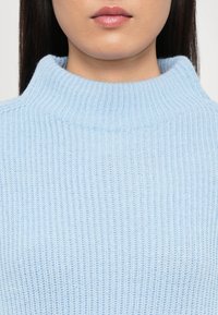 Heled sinine soonikuga turtleneck sveter, millel on kõrge krae ja pehme, tekstuurne kangas, rõhutades keha lähedast sobivust.