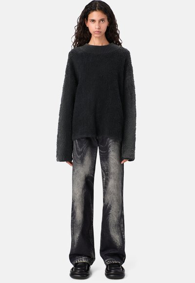 Suéter de punto negro y esponjoso con mangas largas y holgadas, combinado con jeans negros de cintura alta que presentan un patrón más claro y texturizado. Zapatos negros gruesos.