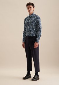 Camicia aderente a maniche corte di colore blu scuro con un intricato motivo paisley, abbinata a pantaloni a vita alta color navy e scarpe in pelle nere.