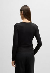 Maglietta nera a maniche lunghe con un design aderente. Presenta una scollatura rotonda e dettagli con bottoni sulle spalle. Tessuto liscio e elasticizzato.