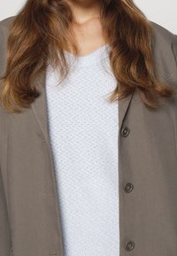 Ljusgrå blazer över en texturerad, ljusblå tröja. Blazern har mörka knappar och ett slätt tyg, medan tröjan har ett stickat mönster.