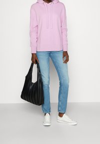 Light pink hoodie with drawstrings, paired with light blue jeans and white sneakers. Black pleated handbag adds texture and contrast.