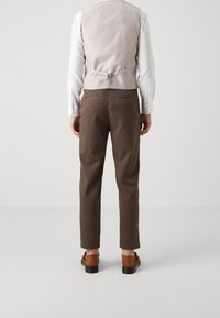 Light gray vest over a white shirt, paired with brown trousers and brown footwear. The vest features a back strap and smooth texture.