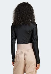 Svart langermet topp med en glatt tekstur, kombinert med beige høyt liv, løstsittende bukser med bred midjeband.