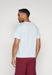 Γαλάζιο κοντομάνικο πουκάμισο από λεία ύλη, με στρογγυλή λαιμόκοψη και αντίθετο μπορντώ σορτς, που αναδεικνύει τις ραφές και τις λεπτομέρειες των ραφών.