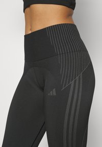Black leggings featuring a high waistband, textured fabric, and subtle vertical stripes, with a smooth finish and a close-fit design.