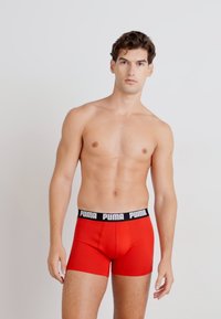Boxerii roșii cu un elastic negru Puma. Țesătura pare netedă și ajustată, punând în evidență designul și silueta.
