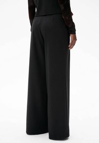 Zwarte wijde broek van een zachte stof, met een op maat gemaakte pasvorm, elegante lijnen en subtiele zakdetails.
