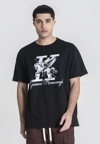 Černé bavlněné tričko s velkým bílým grafikou, na které je zobrazeno křídlaté hřebce, písmeno 'K' a jméno "Gianni Kavanagh" ve stylizovaném písmu.