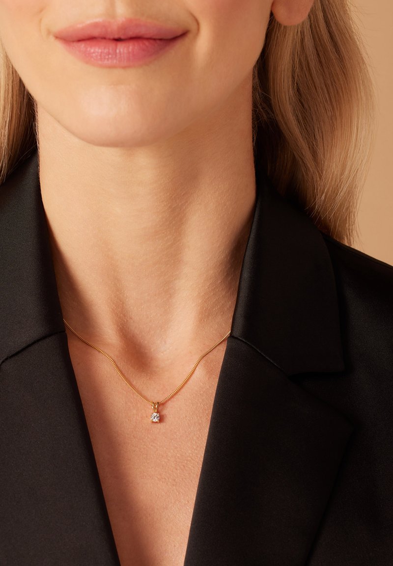 Collier en chaîne dorée avec une texture fine et lisse et un pendentif en diamant transparent, porté sur un vêtement noir à col.