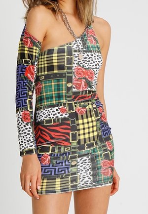 Mujer con un vestido mini de un solo hombro con patrones de patchwork de cuadros, estampado animal, rosas rojas y cinturones negros.