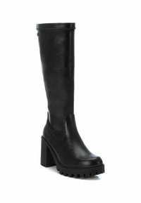 Botas de cuero negro hasta la rodilla con una suela de plataforma gruesa y tacón cuadrado, con paneles laterales elásticos para facilitar su uso.