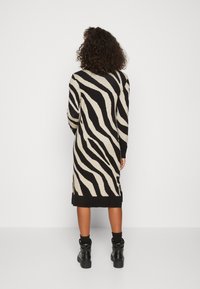 Knä-lång svart och beige zebra-mönstrad stickad klänning med långa ärmar och sidoklyftor; matchas med svarta ankelstövlar.