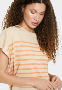 Beige gebreid top met oranje horizontale strepen, ontspannen korte mouwen, ronde halslijn en een zachte textuur.