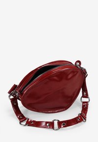 Bolso circular de imitación cuero rojo con cierre de cremallera, textura brillante y una correa con herrajes metálicos y acentos circulares.