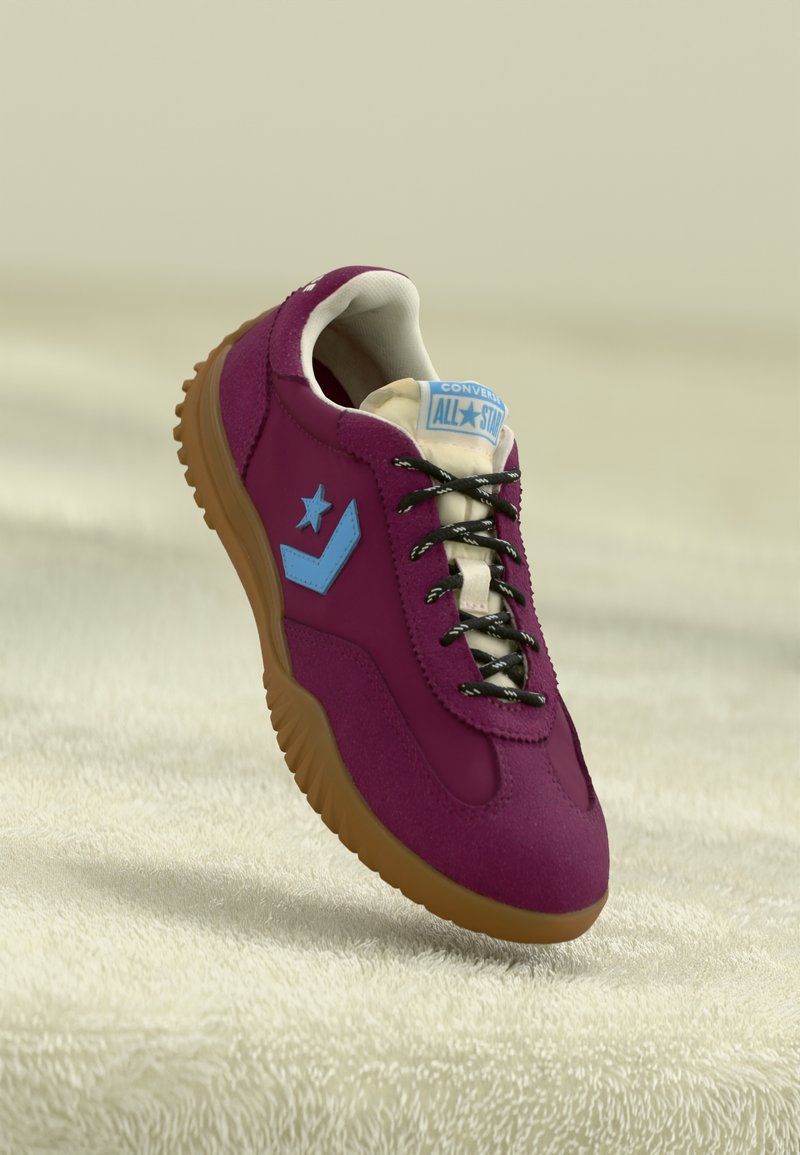 Purple sneaker with a suede-like texture, blue star and chevron accents, black laces, and a gum rubber sole, displayed on a light background.