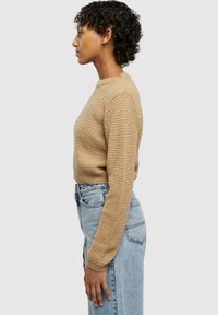 Beige knitted sweater with a textured pattern, round neckline, and long sleeves, paired with light blue high-waisted jeans.