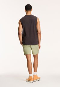 Ärmeloses mørkt top med rund halsudskæring, lysgrønne shorts og orange høj-top sneakers. Glat tekstur, afslappet design.
