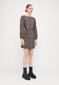 Leopardmønstret kjole med lange ærmer og indsnøret talje. Bæres med sorte ankelstøvler og hvide sokker. Glat stof, afslappet pasform.