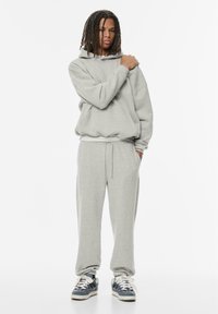 Grijze hoodie met een losse pasvorm, sweatpants met verstelbare tailleband en blauwe sneakers. Het materiaal lijkt zacht met een ontspannen, casual ontwerp.