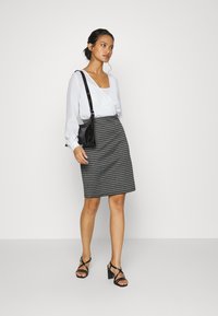 Saia de padrão pied-de-poule preto e branco combinada com uma blusa branca e uma bolsa preta, complementada por sandálias de salto alto pretas com tiras.
