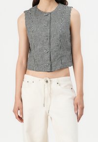 Svart och vit rutigt crop top med ärmlös design, med knappar fram och rak fåll. Kombineras med högmidjade ljusa byxor.