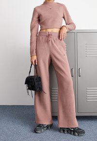 Rosa co-ord-set i texturerat tyg: kort topp med långa ärmar och hög halsringning, tillsammans med vida byxor; svart väska och sneakers.