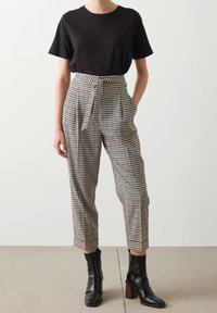 Černé tričko s kulatým výstřihem v kombinaci s vysokým pasem kostkovanými kalhotami s předními kapsami a zavazováním v pase, doplněné černými kotníkovými botami.