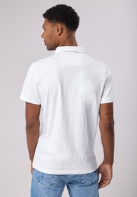 Bílá polo košile s krátkým rukávem a texturovaným povrchem, s klasickým límcem a jemným designem zadního yoke. Nosit s světle modrými džíny.