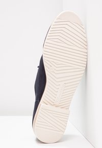 Baskets en daim noir avec semelle en caoutchouc blanc présentant un motif de semelle texturé, taille 37 indiquée sur le talon, et éléments de design minimalistes.