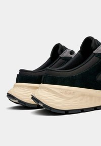 Baskets noires avec une finition en daim lisse, semelle texturée et semelle intermédiaire beige. Comprend des accents gris et un design moderne et épuré.