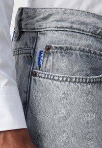 Lys grå denimjeans med rett passform, med en liten frontlomme, merkede etikett og metallbeslag på midjebåndet.