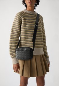 Vævet sort læder crossbody taske med en glat finish, rektangulær form, tynd justerbar rem og kontrasterende hvide syninger.