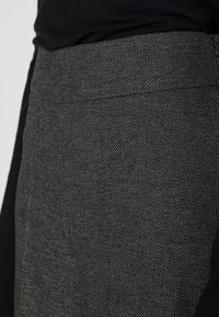 Szary tkany materiał z teksturowanym wzorem, z gładkim czarnym akcentem. Projekt ma dopasowany kształt z subtelnymi szwami.