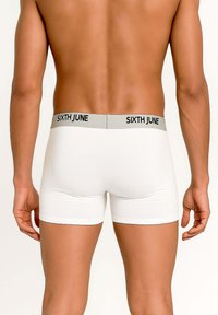 Widok z tyłu na męskiego modela w białych bokserkach z szarym pasem i napisem „SIXTH JUNE” w czarnych literach.
