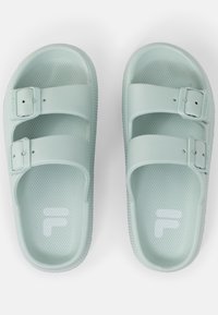 Sandali in plastica verde chiaro con due cinturini regolabili, suola testurizzata e logo bianco. Presentano una suola piatta e bordi arrotondati.