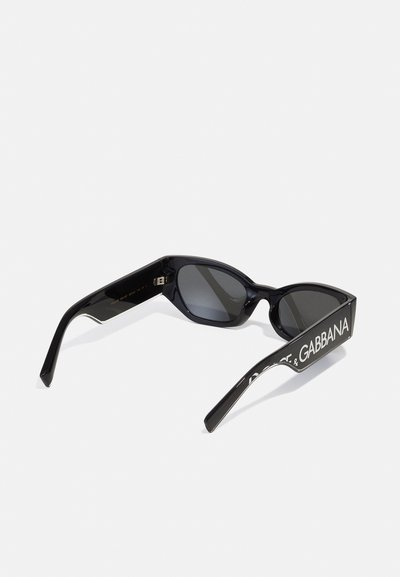 Occhiali da sole neri in plastica con forma a occhio di gatto, lenti scure e lettering bianco a contrasto del brand sulle aste. Texture liscia e lucida.