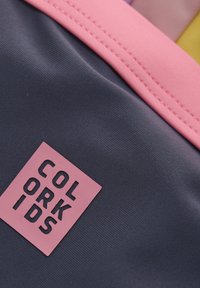 Rucksack aus dunkelgrauem Stoff, mit rosa Akzenten und einem strukturierten Logo-Patch mit der Aufschrift "COLOR KIDS". Verfügt über glatte Nähte und ein einfaches Design.