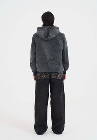 Sudadera gris con capucha y bordado intrincado de dragón, combinada con pantalones anchos negros que presentan patrones dorados detallados y acentos desgastados.