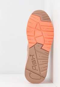 Sula i ljusbrun och korall med texturerat greppmönster; har varumärket "ASH" och storlek "38" präglat på sidan.