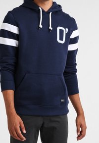 Sudadera azul marino de mezcla de algodón, con un bolsillo frontal, acentos de rayas blancas en las mangas y un logotipo en contraste en el pecho.