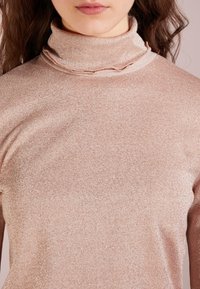 Přiléhavý svetr s rolákem ve starorůžové barvě, vyrobený z texturované, třpytivé látky s volánkovým detailem na krku. Jednoduché dlouhé rukávy.